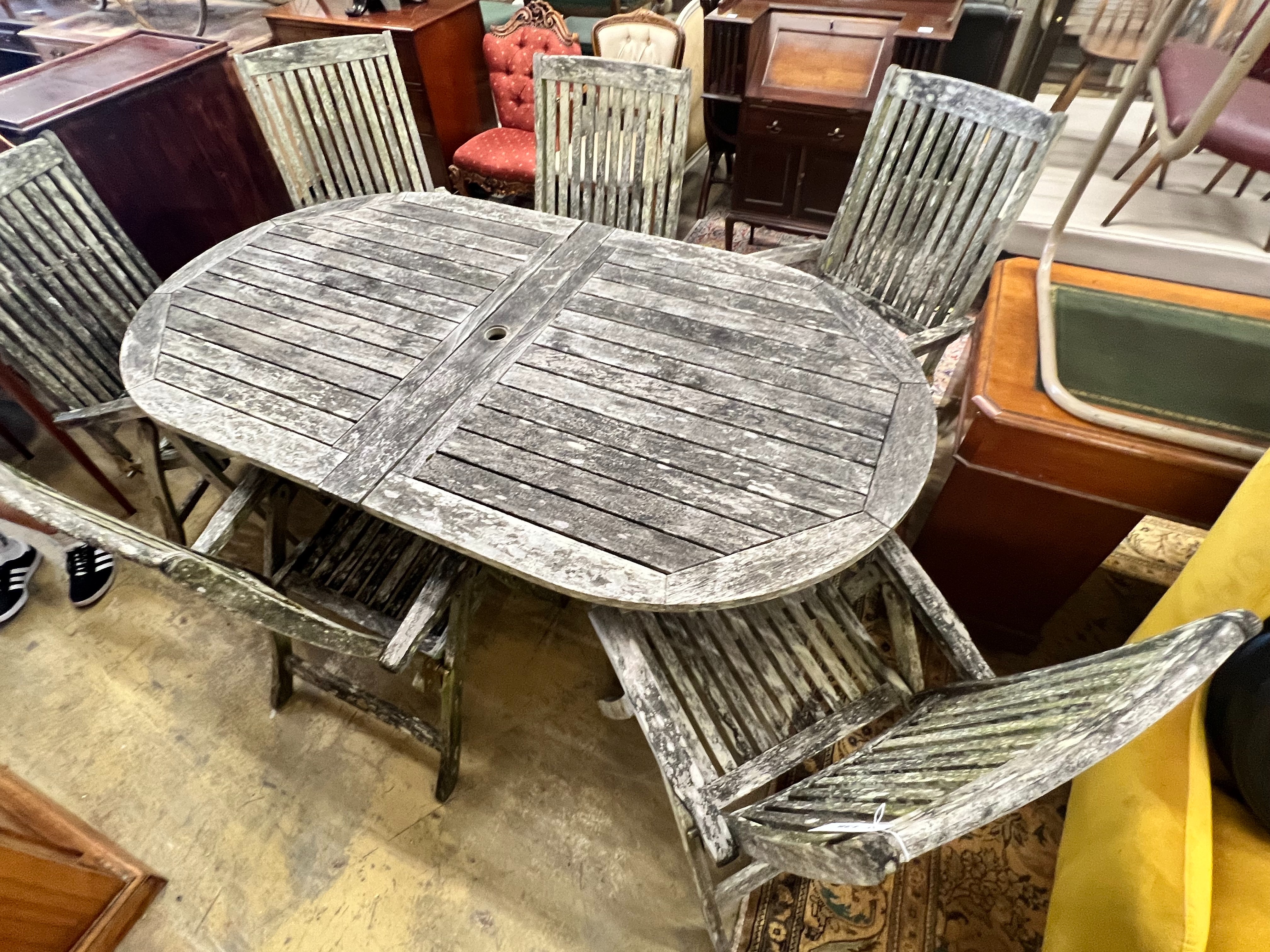 A weathered teak oval extending garden table, extended 250cm width 109cm height 73cm, and six folding garden elbow chairs